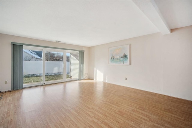 spare room featuring beam ceiling and light hardwood / wood-style flooring