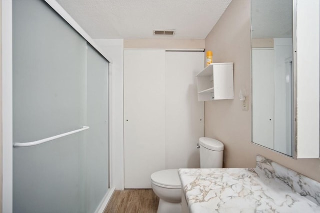 bathroom featuring an enclosed shower, vanity, a textured ceiling, hardwood / wood-style floors, and toilet