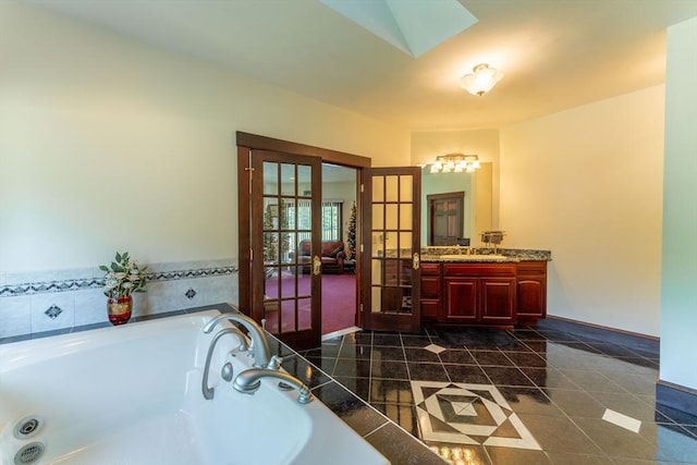 bathroom featuring a relaxing tiled tub, vanity, a skylight, and french doors