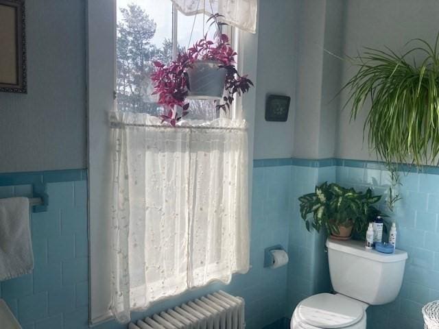 bathroom featuring radiator heating unit, a healthy amount of sunlight, tile walls, and toilet