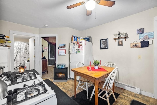 dining area with ceiling fan, a baseboard radiator, a fireplace, baseboards, and stone finish floor