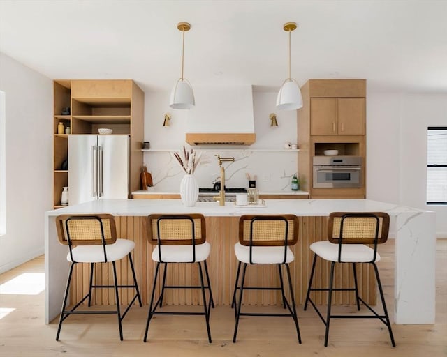 kitchen featuring appliances with stainless steel finishes, a breakfast bar, light wood-type flooring, and decorative light fixtures