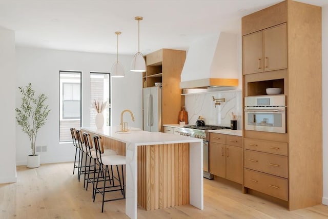 kitchen featuring light hardwood / wood-style flooring, premium range hood, a kitchen island with sink, high quality appliances, and light brown cabinetry