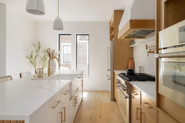 kitchen with light hardwood / wood-style floors, high end stove, custom range hood, an island with sink, and decorative light fixtures