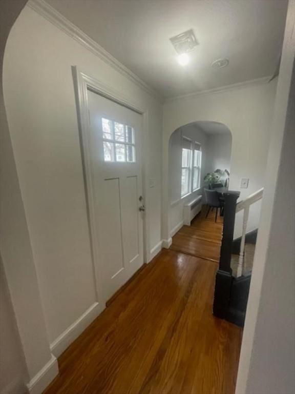 foyer featuring arched walkways, baseboards, ornamental molding, and wood finished floors