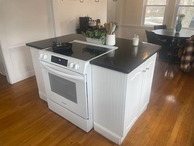 kitchen featuring white cabinetry, white range with electric stovetop, dark countertops, and wood finished floors