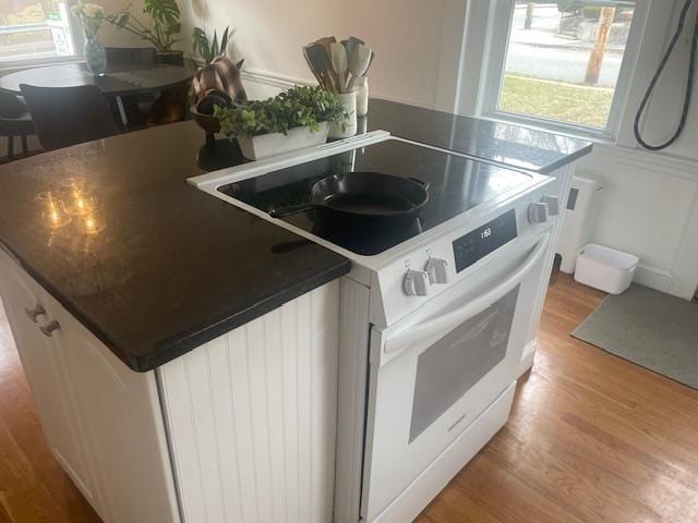 kitchen with a kitchen island, dark countertops, white electric range oven, and light wood-style floors