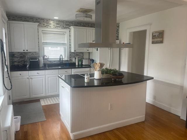 kitchen featuring white cabinetry, island range hood, wood finished floors, and a sink