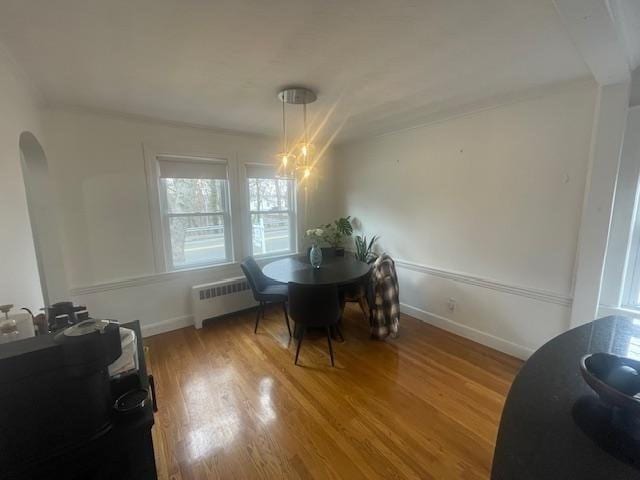 dining space with light wood finished floors, radiator, a notable chandelier, and arched walkways