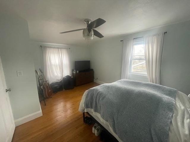 bedroom with multiple windows, wood finished floors, and baseboards