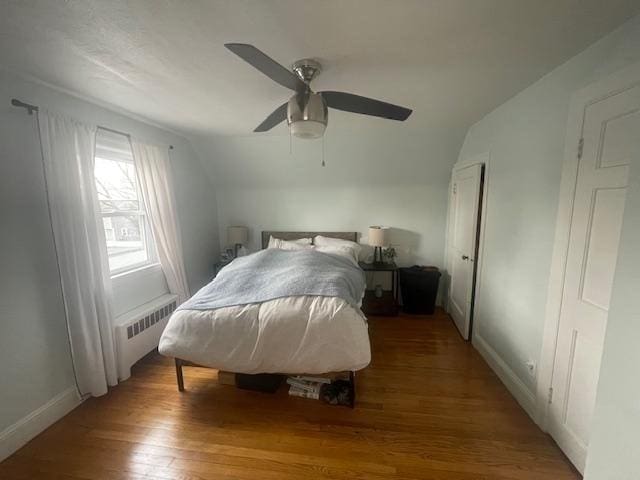 bedroom featuring a ceiling fan, radiator heating unit, lofted ceiling, light wood-style flooring, and baseboards