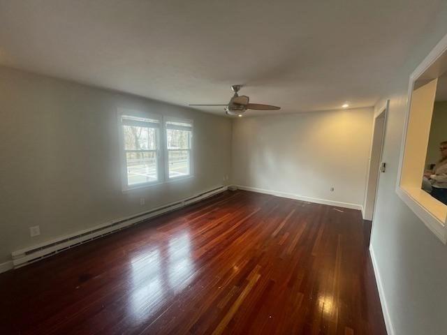 empty room with a ceiling fan, wood finished floors, baseboards, and baseboard heating