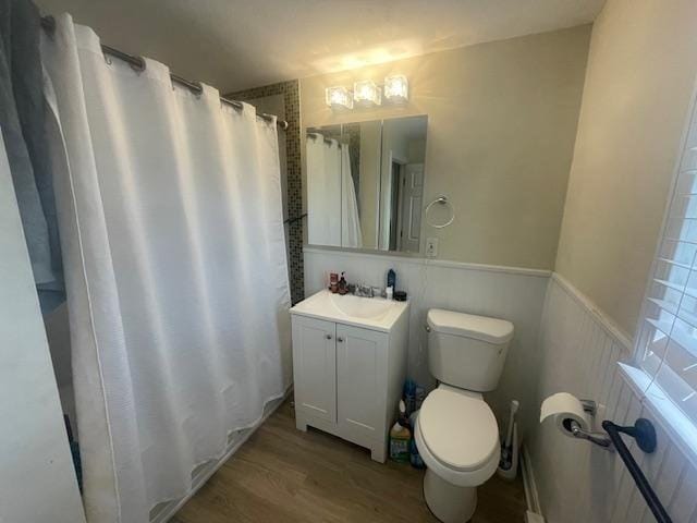 bathroom featuring vanity, toilet, a shower with shower curtain, a wainscoted wall, and wood finished floors