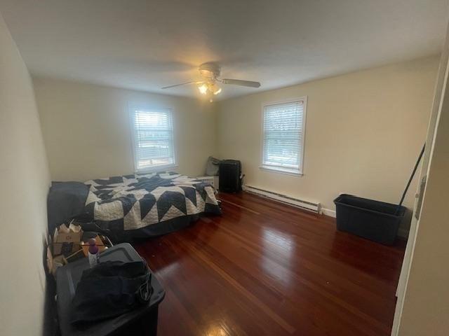 bedroom with a ceiling fan, wood finished floors, multiple windows, and baseboard heating