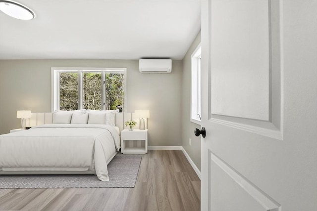 bedroom featuring baseboards, a wall mounted AC, and wood finished floors
