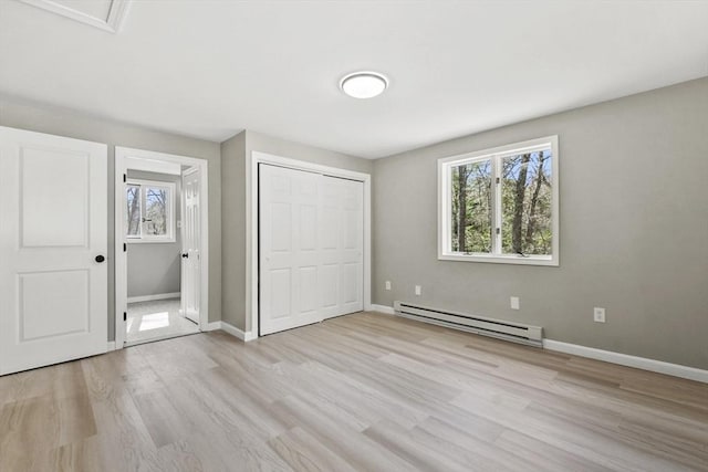 unfurnished bedroom featuring a closet, a baseboard radiator, multiple windows, and light wood finished floors
