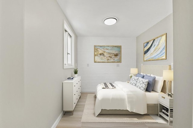 bedroom with baseboards, light wood-style flooring, and an accent wall