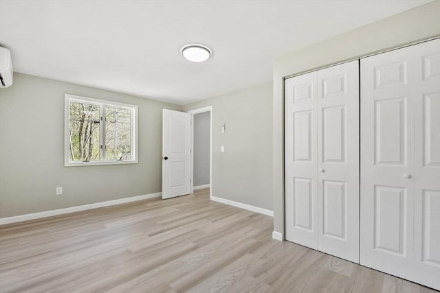 unfurnished bedroom with light wood-type flooring, baseboards, a wall mounted AC, and a closet