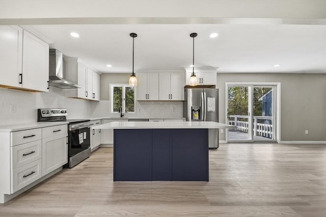kitchen featuring wall chimney range hood, a kitchen island, backsplash, light wood-style floors, and stainless steel appliances
