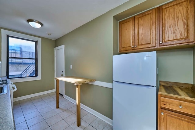 kitchen with white fridge, light tile patterned flooring, and range