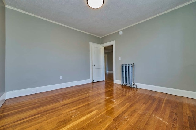 empty room with radiator, hardwood / wood-style floors, a textured ceiling, and ornamental molding