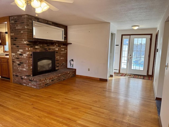 unfurnished living room with ceiling fan, a brick fireplace, baseboard heating, light hardwood / wood-style flooring, and a textured ceiling