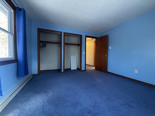 unfurnished bedroom with dark colored carpet, multiple closets, and a baseboard heating unit