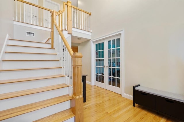 stairway featuring baseboards, visible vents, a towering ceiling, wood finished floors, and french doors