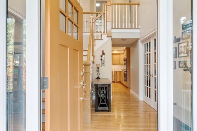 entryway with a towering ceiling, light wood-style floors, stairway, and french doors