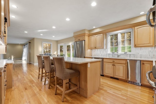 kitchen with a center island, appliances with stainless steel finishes, a sink, light stone countertops, and light wood-type flooring