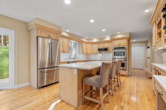 kitchen with light wood finished floors, tasteful backsplash, a kitchen island, appliances with stainless steel finishes, and light brown cabinets