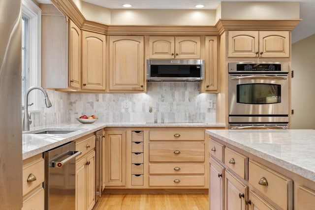 kitchen with appliances with stainless steel finishes, light stone countertops, a sink, and light brown cabinetry