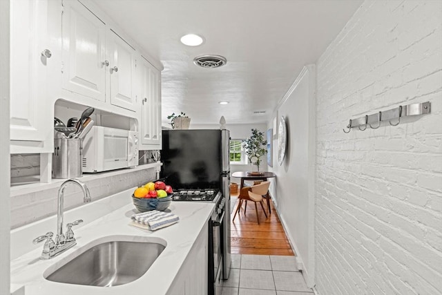 218 Washington St Unit 5, Marblehead, MA 01945 - kitchen with appliances with stainless steel finishes, light tile patterned flooring, white cabinets, a sink, and light stone counters