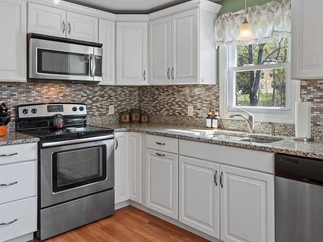 kitchen with light stone counters, a sink, stainless steel appliances, white cabinetry, and decorative backsplash