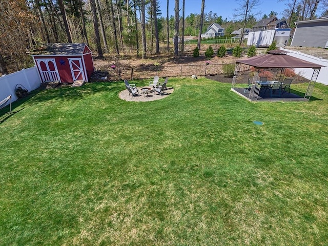 view of yard with a storage shed, an outbuilding, a patio area, a fenced backyard, and a fire pit
