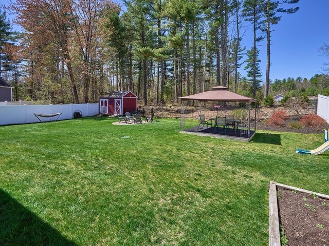 view of yard with a gazebo, a fenced backyard, an outbuilding, and a storage unit
