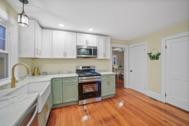 kitchen featuring sink, hanging light fixtures, light hardwood / wood-style flooring, green cabinets, and stainless steel appliances