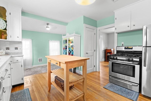 kitchen with appliances with stainless steel finishes, light hardwood / wood-style flooring, white cabinets, and decorative backsplash