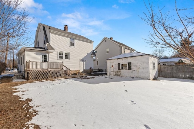 snow covered back of property featuring a wooden deck and an outdoor structure