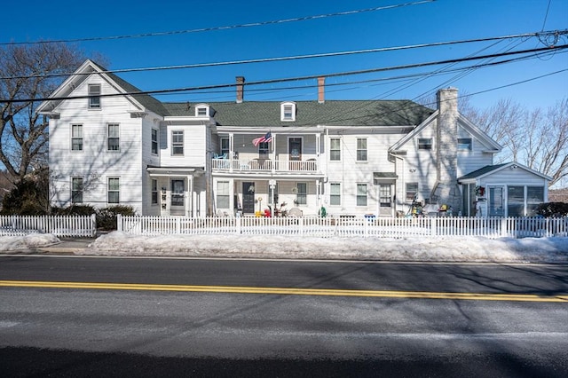 view of front of property with a fenced front yard, a chimney, and a balcony