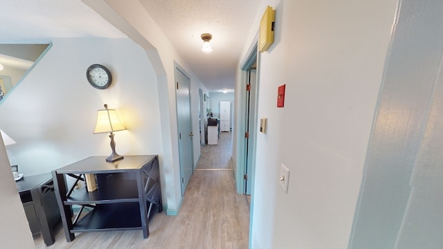 hallway with a textured ceiling and light wood-type flooring