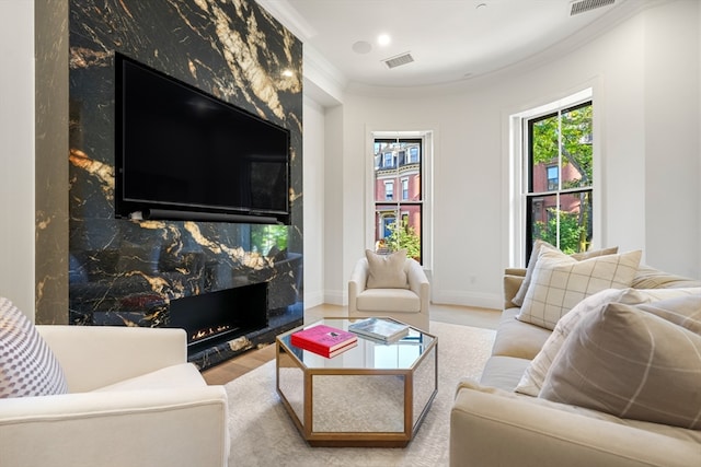 living room with a high end fireplace, crown molding, and light wood-type flooring