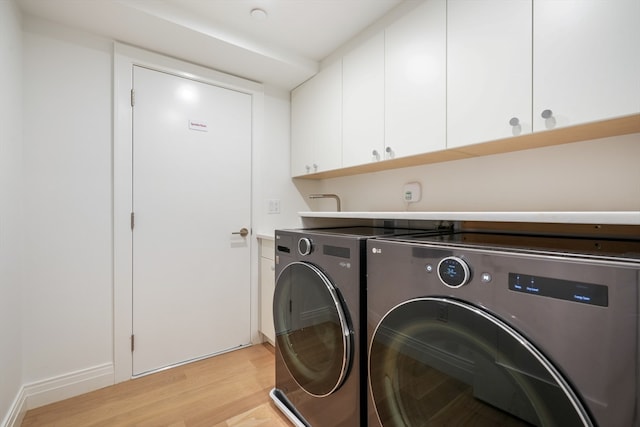 washroom featuring washing machine and dryer, cabinets, and light wood-type flooring