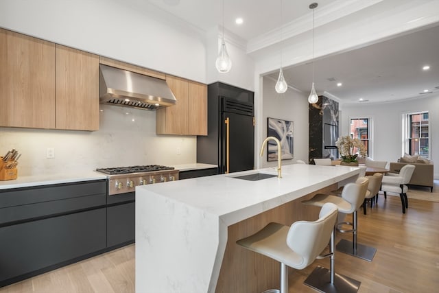 kitchen with wall chimney range hood, a kitchen island with sink, decorative light fixtures, and sink