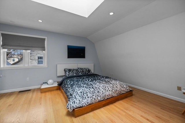 bedroom with vaulted ceiling with skylight, baseboards, wood finished floors, and recessed lighting