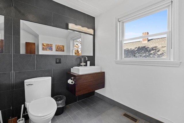 half bathroom with tile walls, visible vents, toilet, vanity, and tile patterned floors