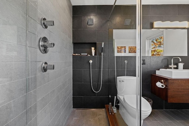 bathroom with toilet, tile walls, tiled shower, and vanity