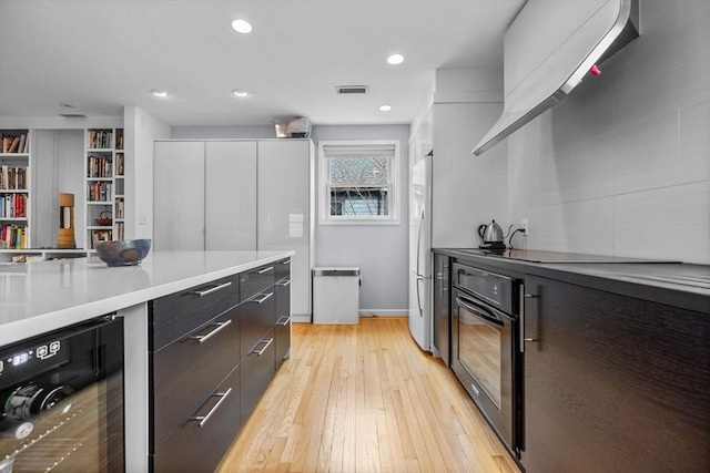 kitchen with light wood finished floors, visible vents, modern cabinets, beverage cooler, and black appliances