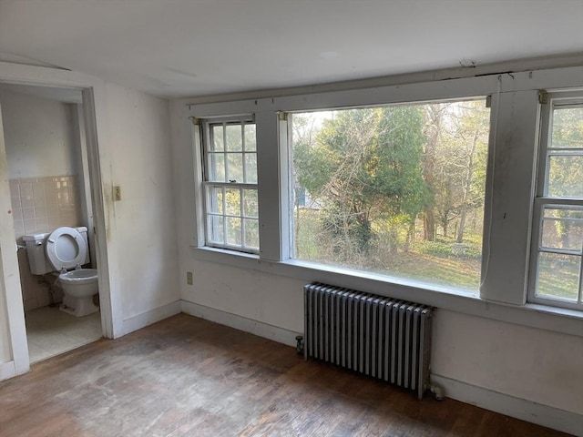 empty room featuring a wealth of natural light, radiator, and dark wood-type flooring