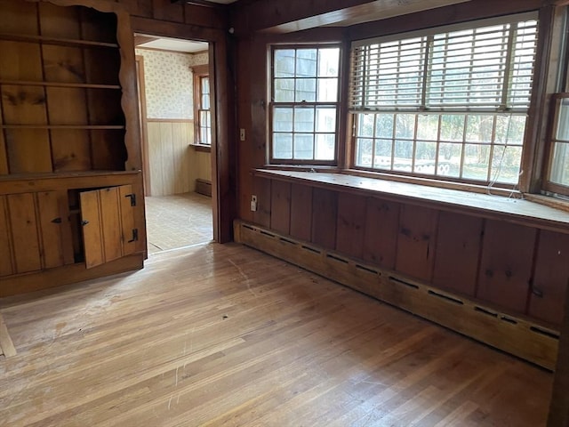 interior space featuring light wood-type flooring, a baseboard heating unit, and wood walls